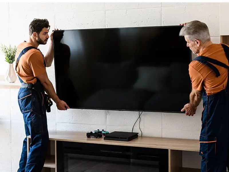 Two professionals mounting a large, flatscreen TV on a wall